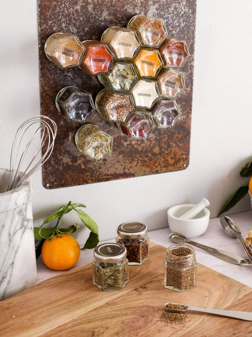 A group of glass spice jars magnetically attached to a steel backsplash in a kitchen