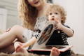 Toddler looking through a colourful picture book while sitting with their mother.