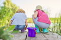 Children enjoying summer themed sensory play with buckets beside a pond.