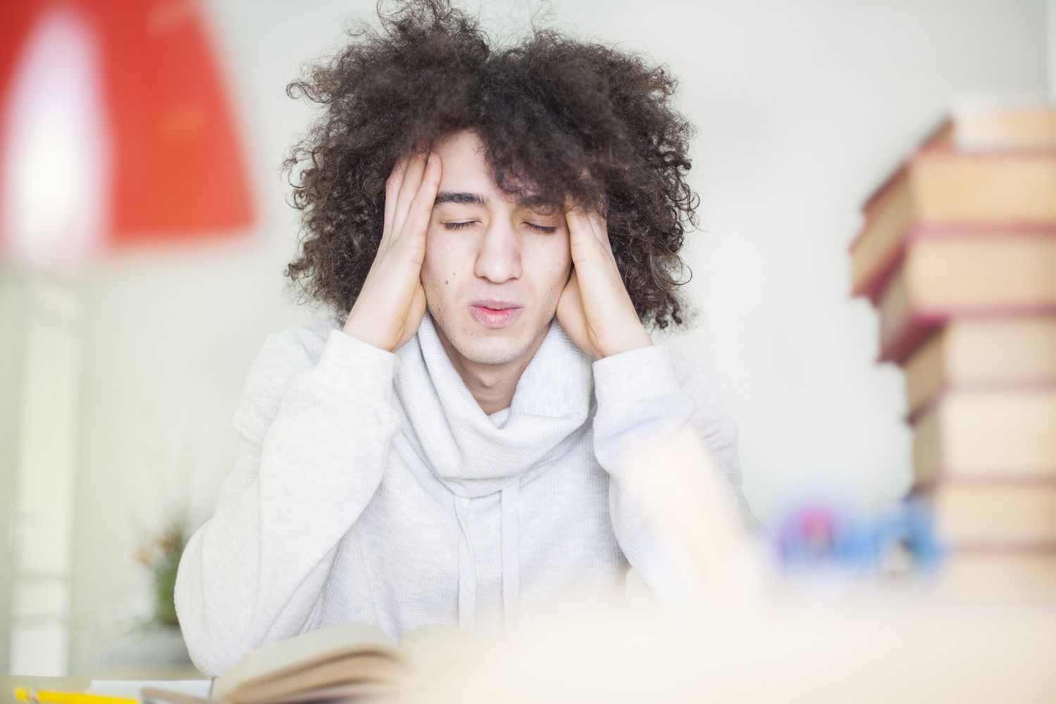 A multi ethnic man with large curly hair has his hands on his temples with a stressed expression on his face.