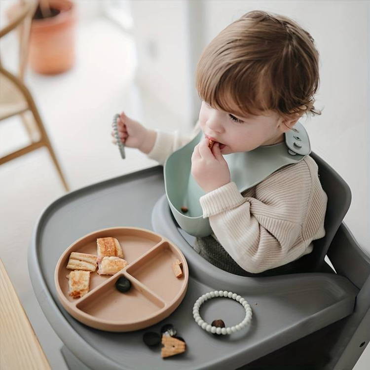 Baby sitting in her lunch chair and feeding herself from the silicone plate.