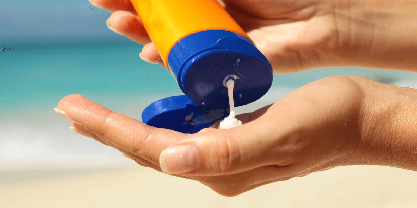 Hands squeezing tube of sunscreen.