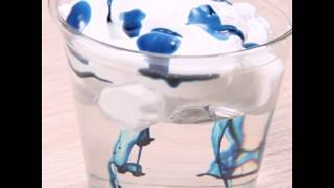 Close up of a glass of water topped with shaving foam and food coloring drops