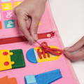 Woman's hand tying shoelaces on a pink activity felt board for children. 