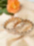 Gold bangles with intricate circular diamond settings placed on a light fabric near an orange rose.