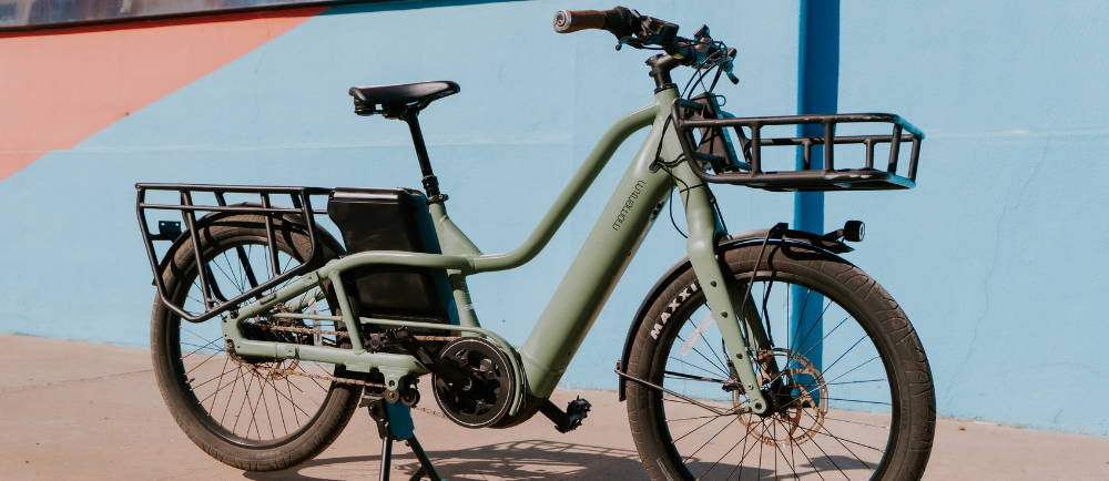 A green Momentum PakYak E+ electric cargo long tail bike in front of a wall