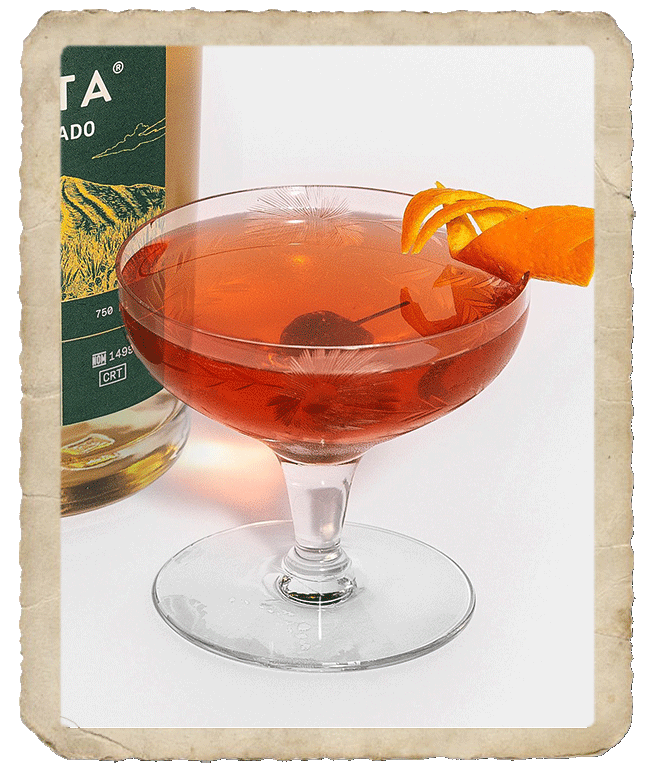 Glass with a dark orange colored prepared cocktail with orange peels