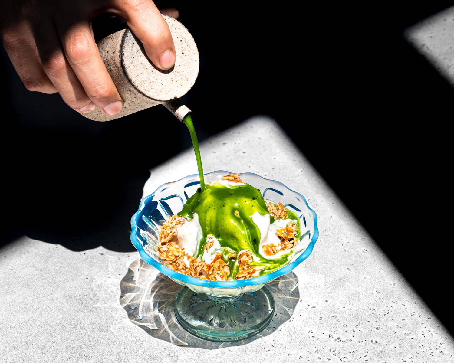 A bright green shot of matcha is drizzled over a scoop of vanilla ice cream with almond praline crumbles.