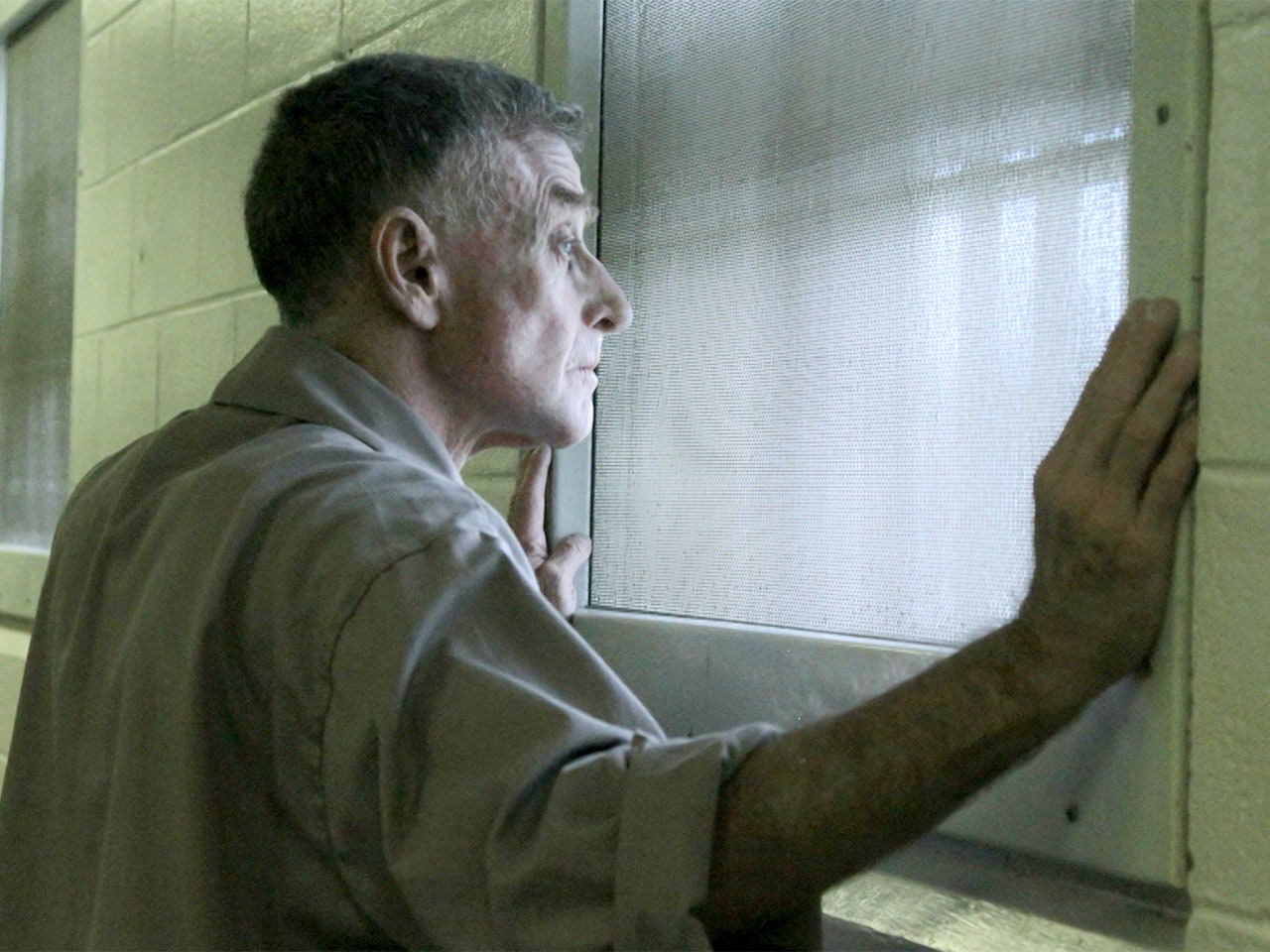 Michael Peterson, standing behind a window in a jail cell looking outside.