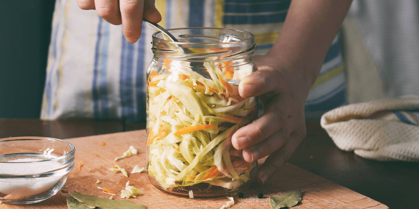 Woman scooping shredded cabbage out of a jar.