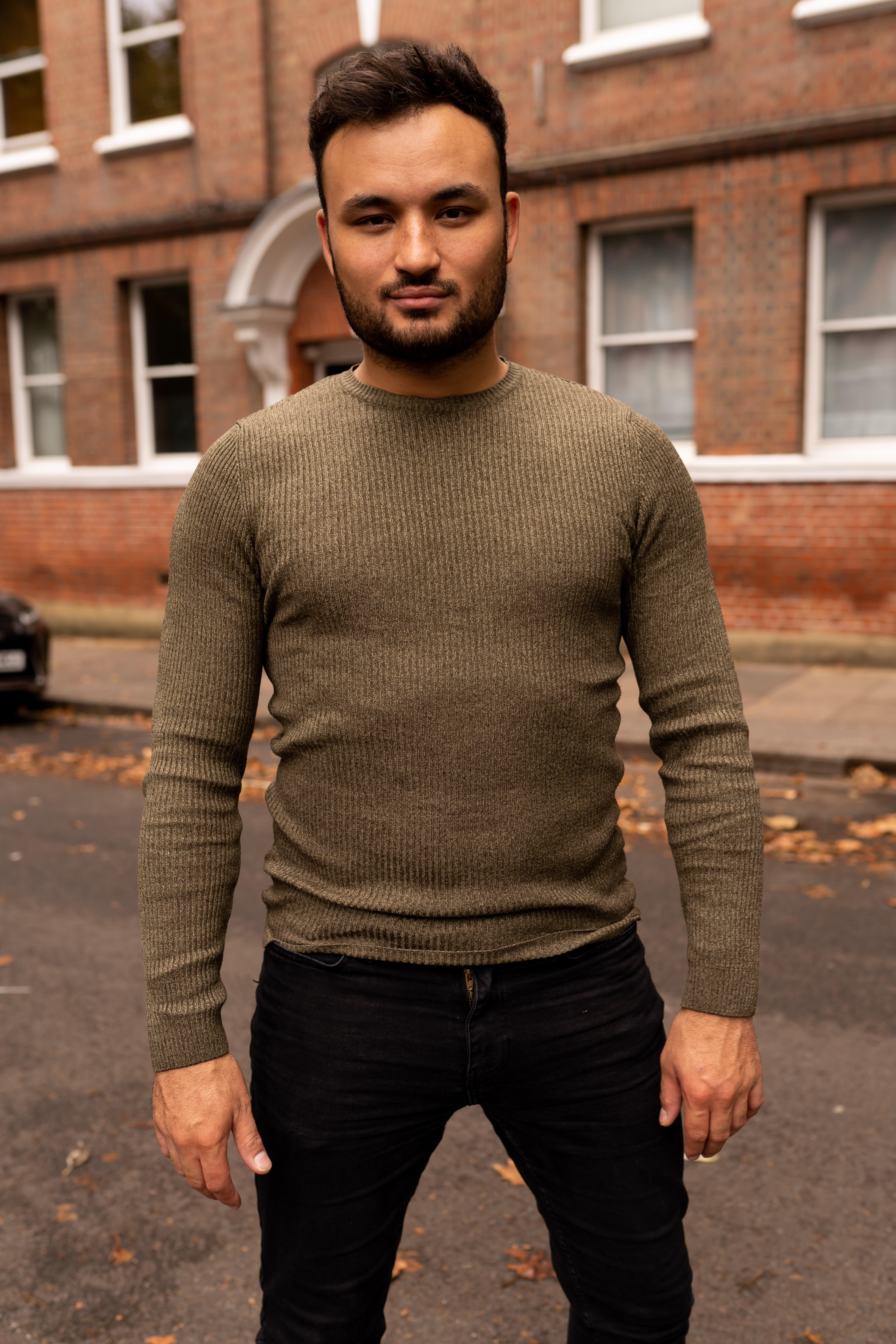 Lewis Oakley standing confidently and smiling against a brick building.