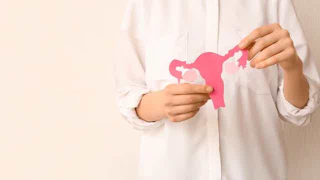 Person in white shirt holding cutouts shaped like two pink figures, resembling a playful puzzle.