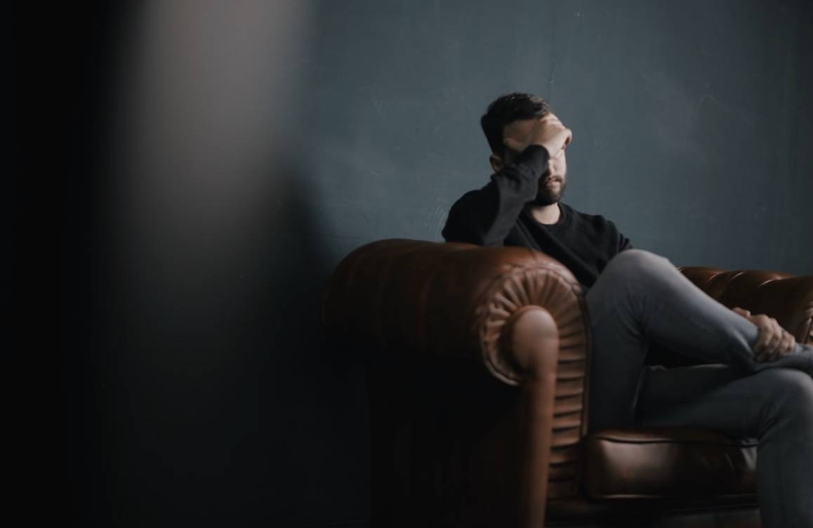  a person sits and holds their head on a sofa