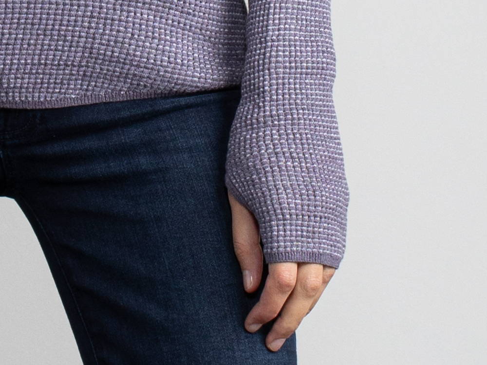 Close up of a woman's hand wearing a purple waffle knit long sleeve shirt.