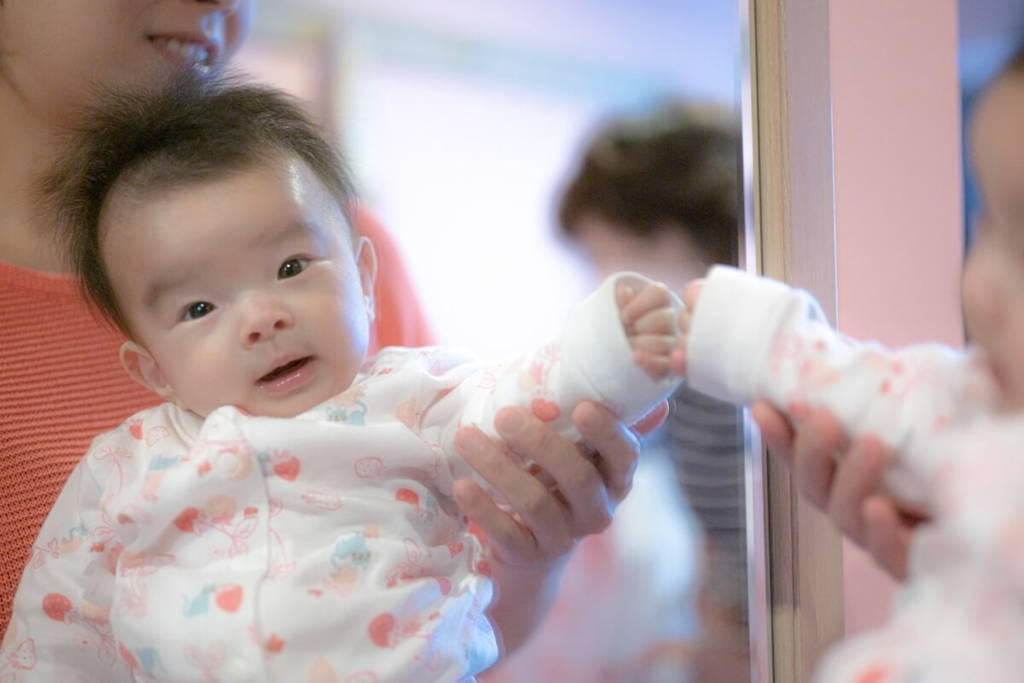 Mother holding a baby that is touching a mirror.