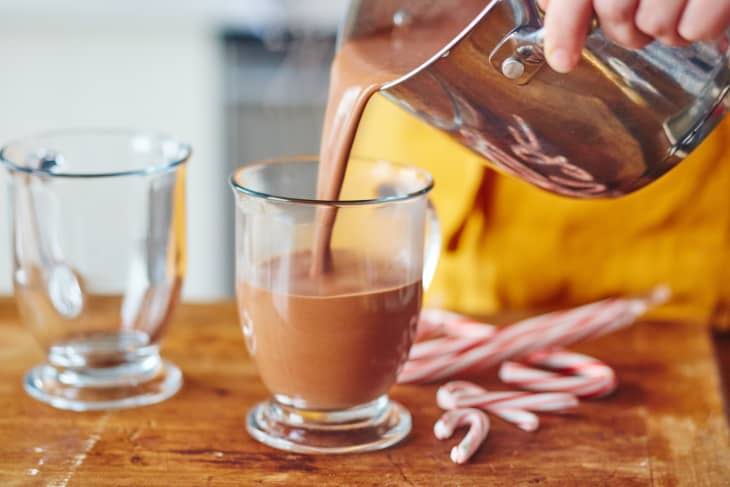 Pouring hot chocolate into a glass with candy canes on the side