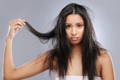 Latin american woman with sad face holding a strand of her frizzy hair in hand