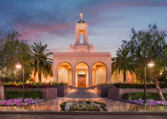 Newport Beach temple glowing against the evening sky. The flowerbeds are full of pastel colored flowers.