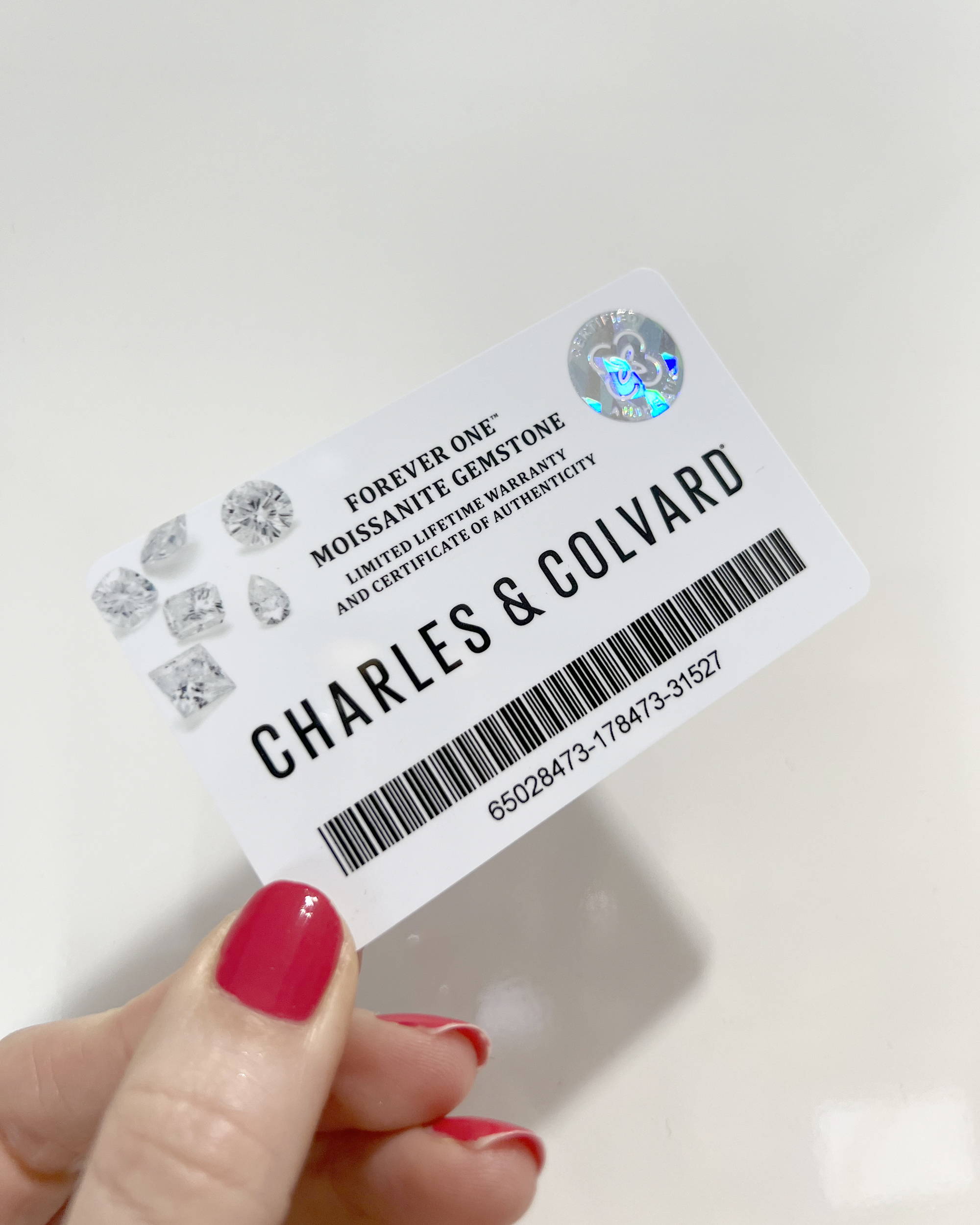 One hand holds the authorized sales card of Charles & Colvard, the largest moissanite manufacturer in the world.