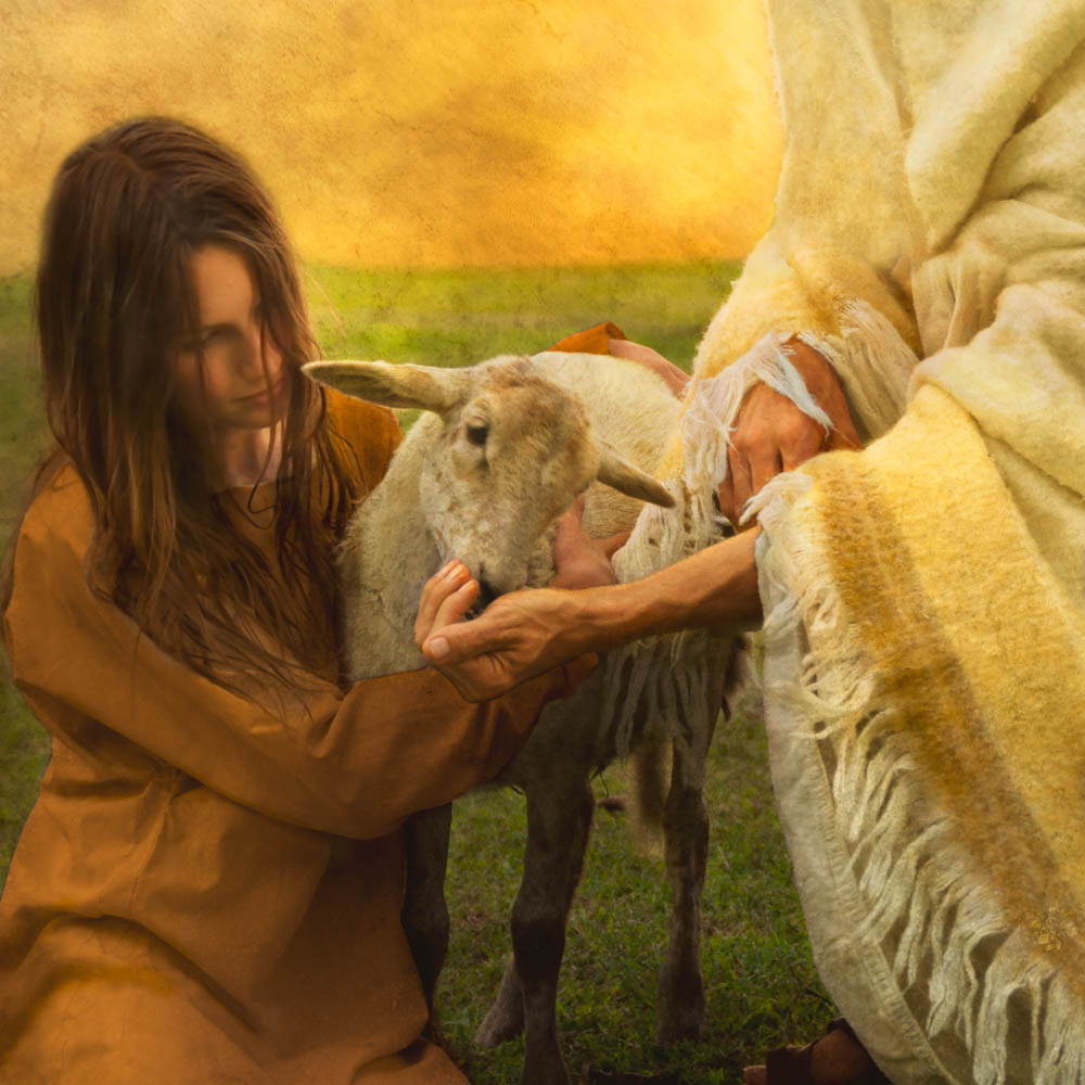 A woman helps Jesus feed a lamb.