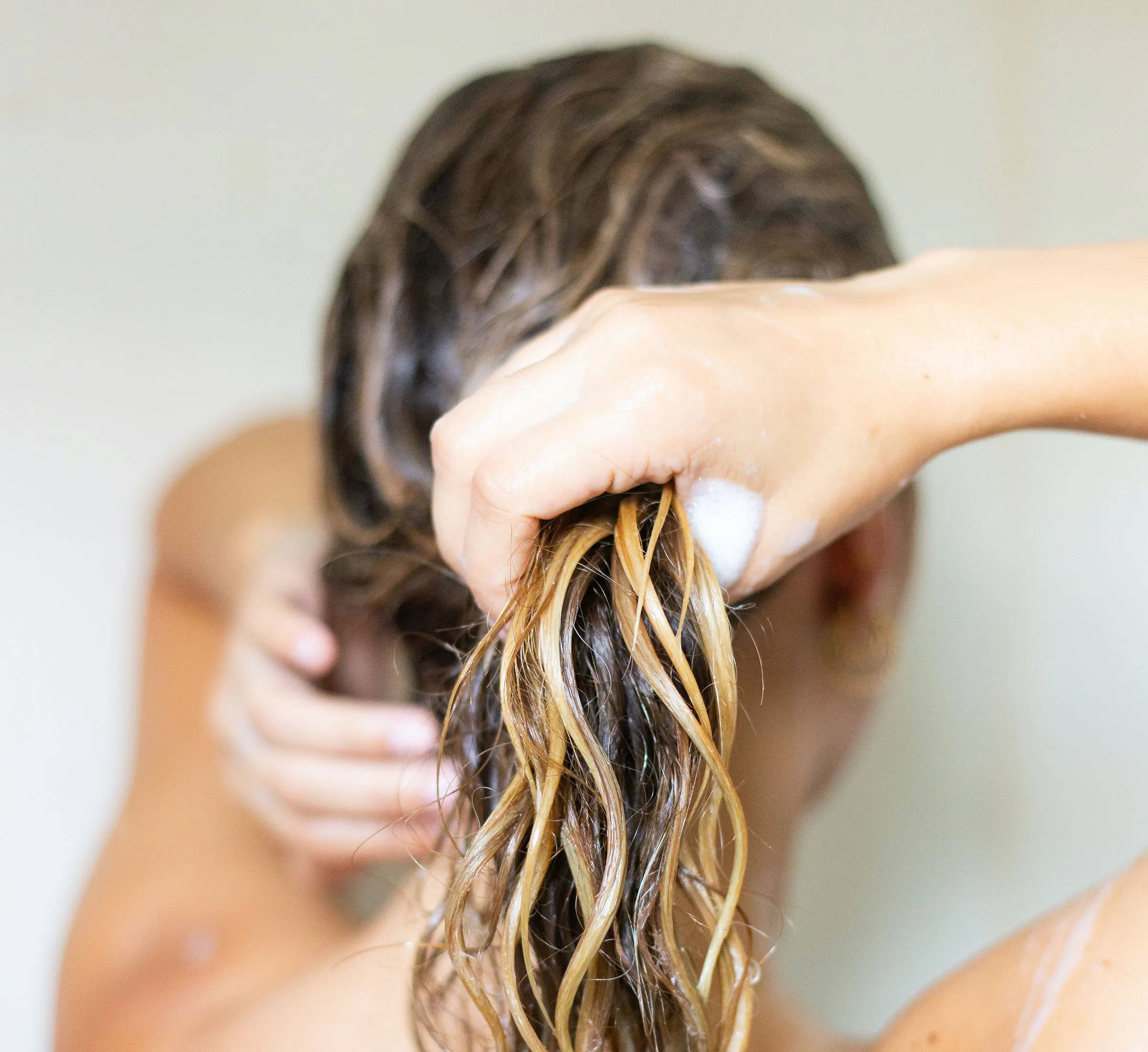 woman with a mix of blonde and brunette hair is rinsing her strands in the shower