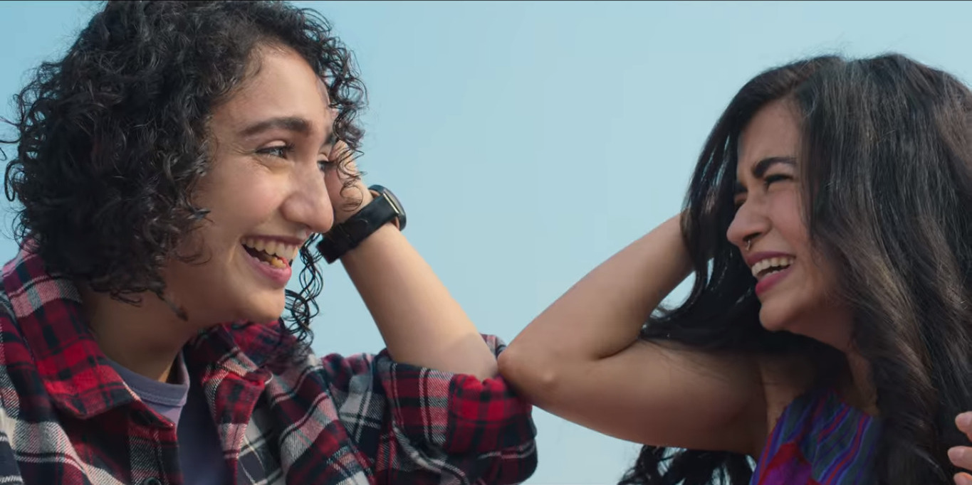 Muskaan and Tarasha laughing together while reclining on a table.