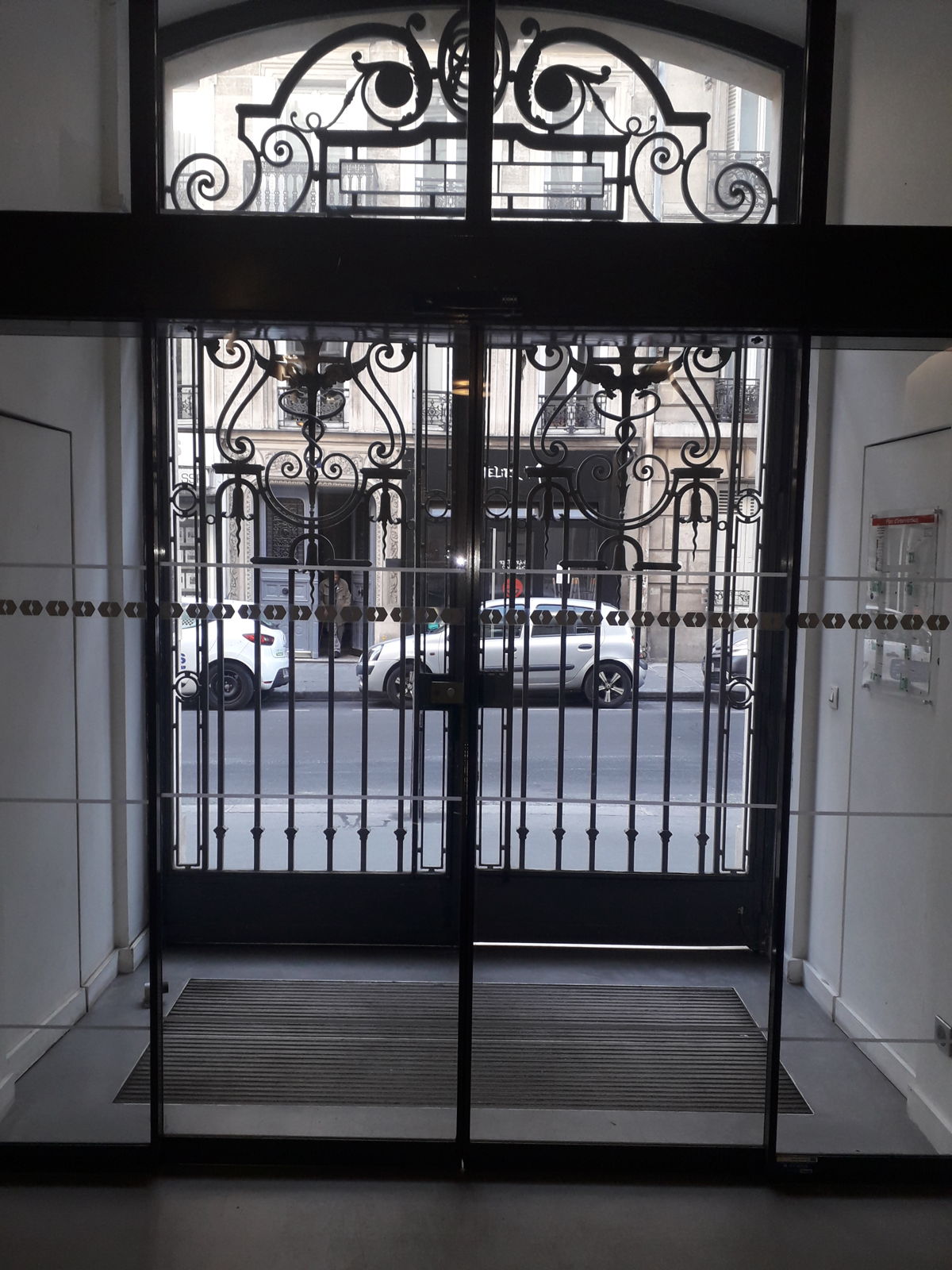Porte automatique vitrée doublée d'une grille en fer forgé dans un hall d'immeuble