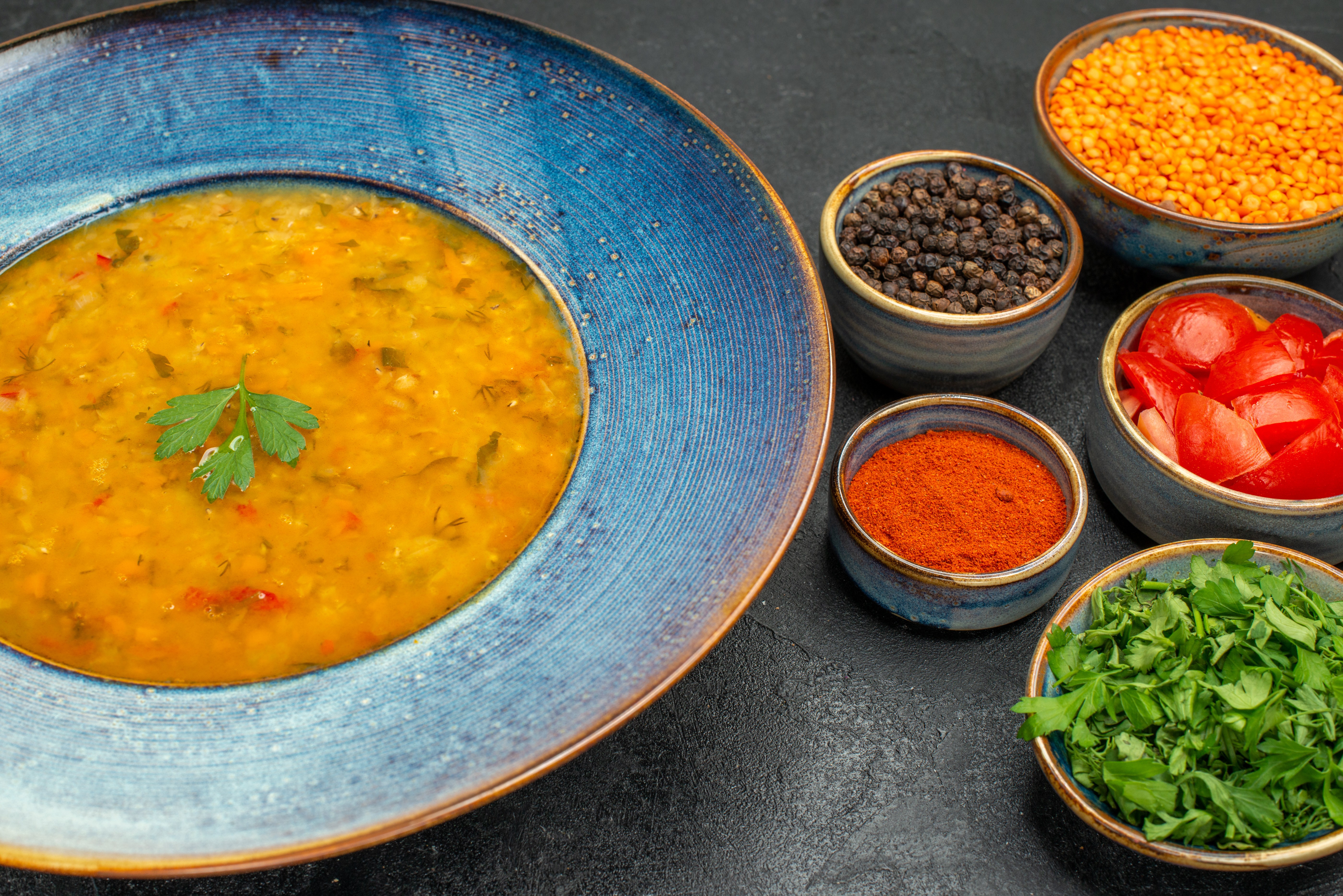 A bowl of Indian curry with a cilantro leaf on top surrounded by Indian curry ingredients