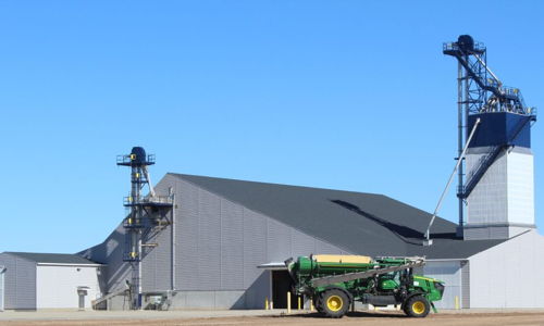 Large agricultural facility with a green tractor, conveying industriousness and modern farming against a clear blue sky.