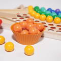 Wooden orange beads placed in a orange silicone cup, with Montessori Rainbow Beads toy in the background.