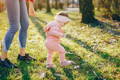 Baby taking first steps outdoors with parent nearby, early walking stage and balance development