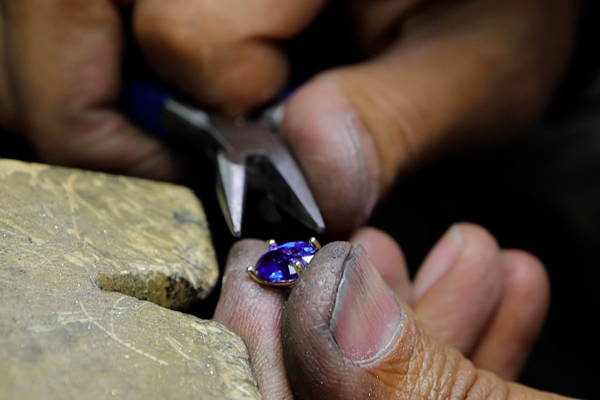 Hands are busy setting a sapphire on the claws of a ring.