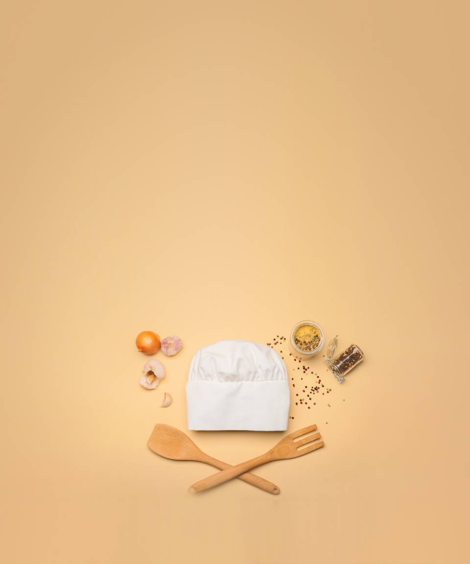 A chefs hat, wooden spatula and fork, onions and garlic, and spilled spices and peppercorns for Confetti's Virtual Cooking Basics Class