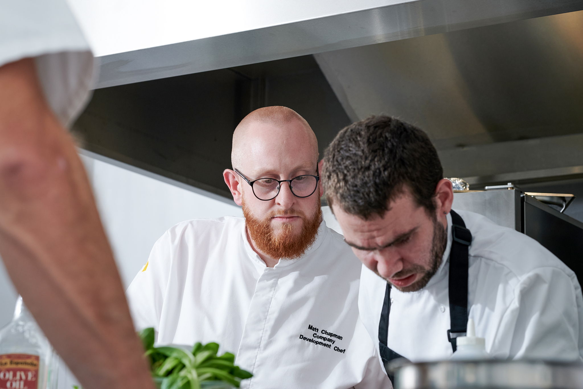 Chef looking over the shoulder of another chef at work.