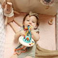 Baby girl lying in her crib and putting a Montessori Silicone Pulling Toy in her mouth. 