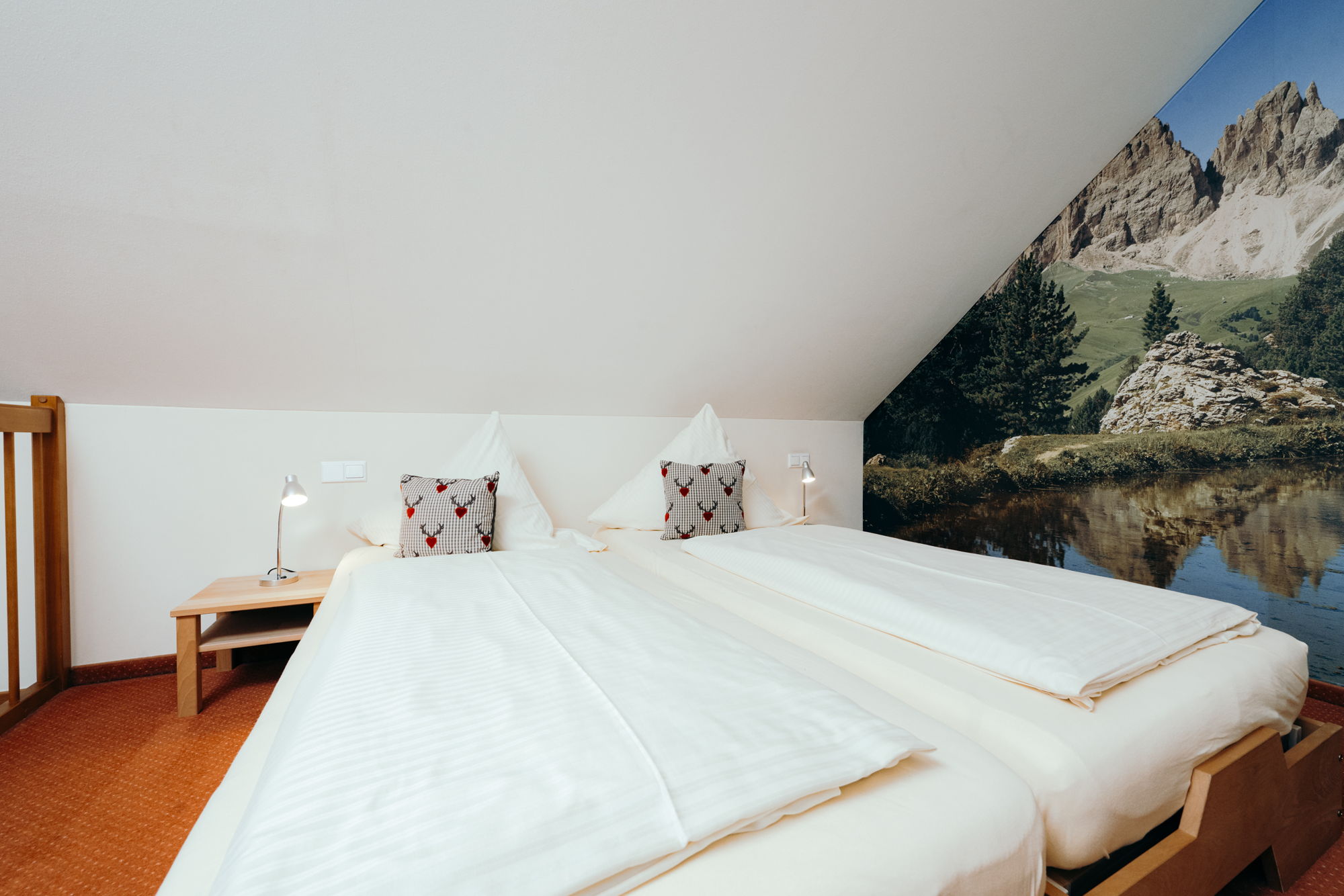 Zwei weiß bezogene Einzelbetten in einem Schlafzimmer mit Dachschräge, im Hintergrund ein buntes Berg Bild.