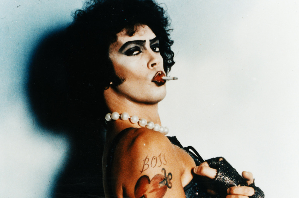 Dr. Frank-N-Furter posing in drag with a cigarette in mouth and a look to t...