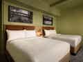 Hotelzimmer mit zwei ordentlich gemachten Queensize-Betten, braunen Kopfteilen, grünen Wänden und schwarz-weißen Wandbildern.