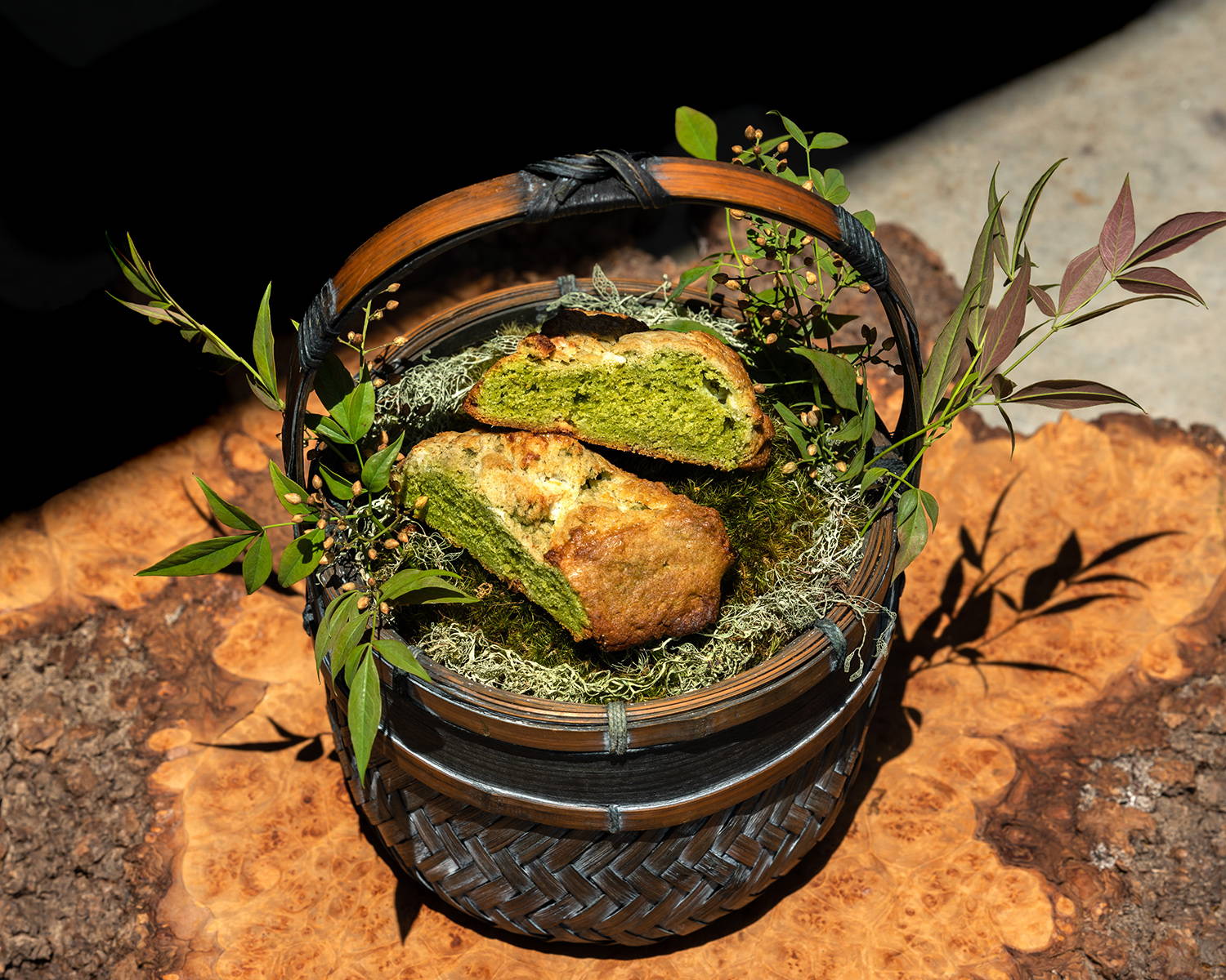 A halved matcha scone, bright green on the inside, sits inside a woven basket.