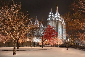 Salt Lake Temple surrounded by snowfall and Christmas lights. 
