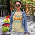 Woman wearing the psychedelic themed shirt "Good Vibes Only" with a jean jacket on top, walking in a city park.