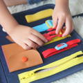 A Montessori Busy Board with the child's hands playing with the buckle. 