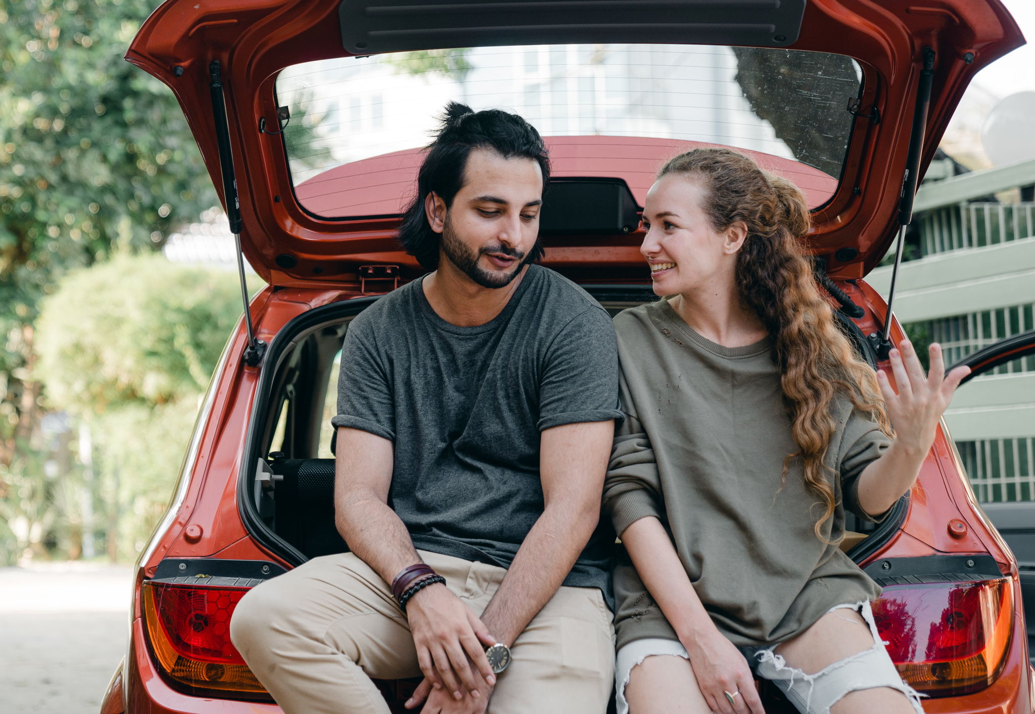 An attractive couple sitting together in the trunk of a car having an intimate conversation.