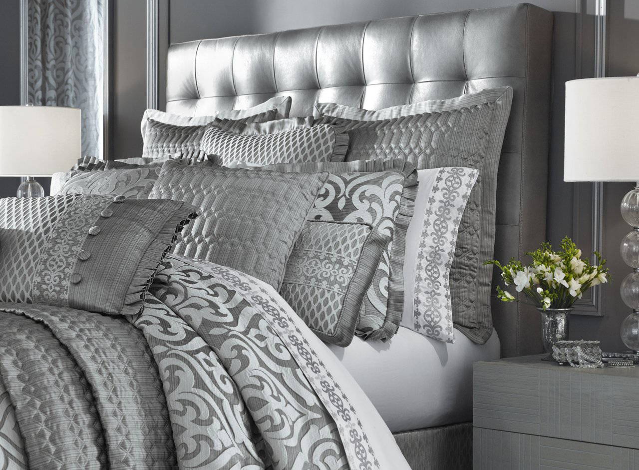 A bed covered in silver J Queen bedspreads and pillows