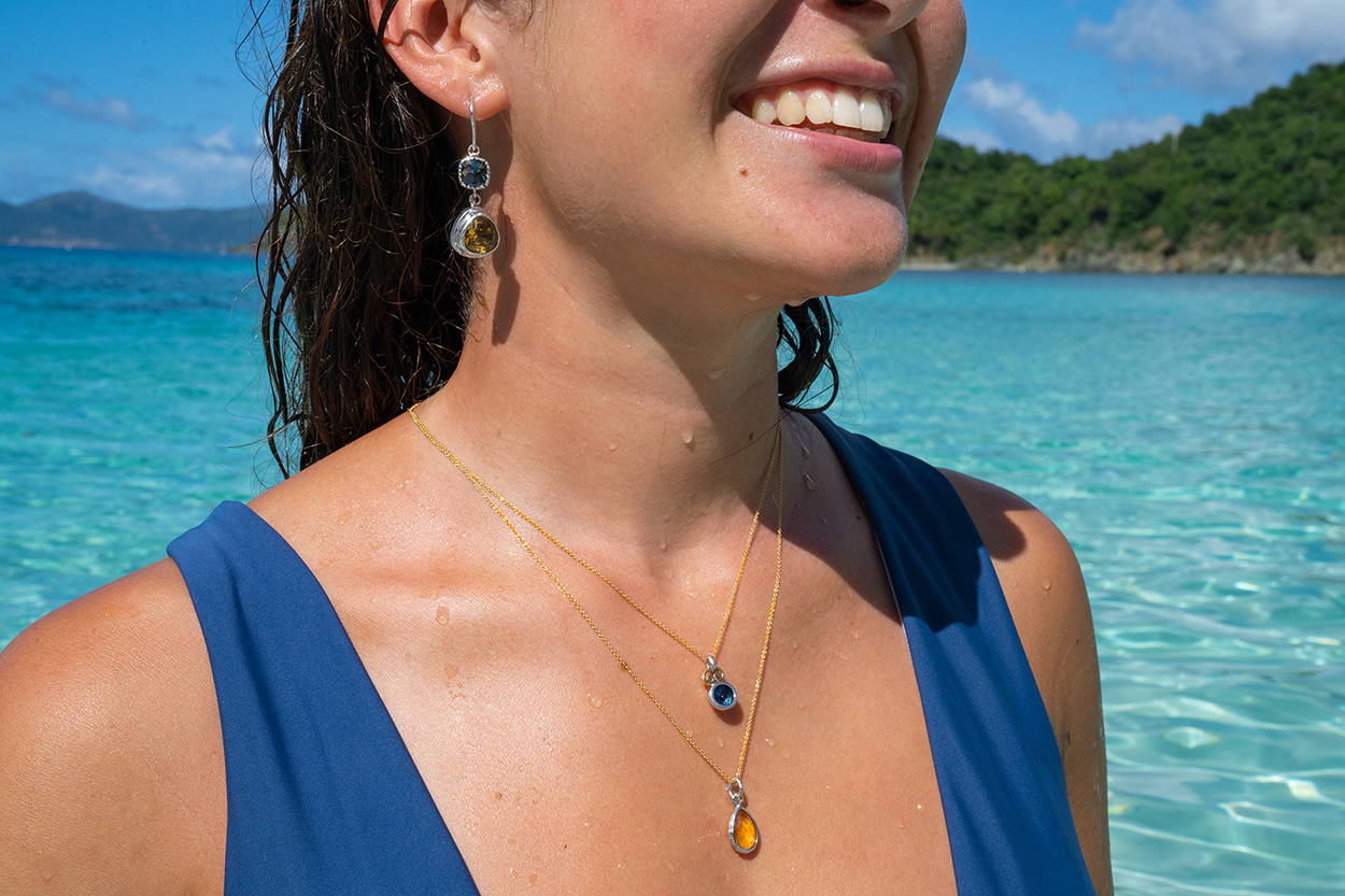 Girl in front of the ocean wearing citrine and blue topaz earrings and pendants.