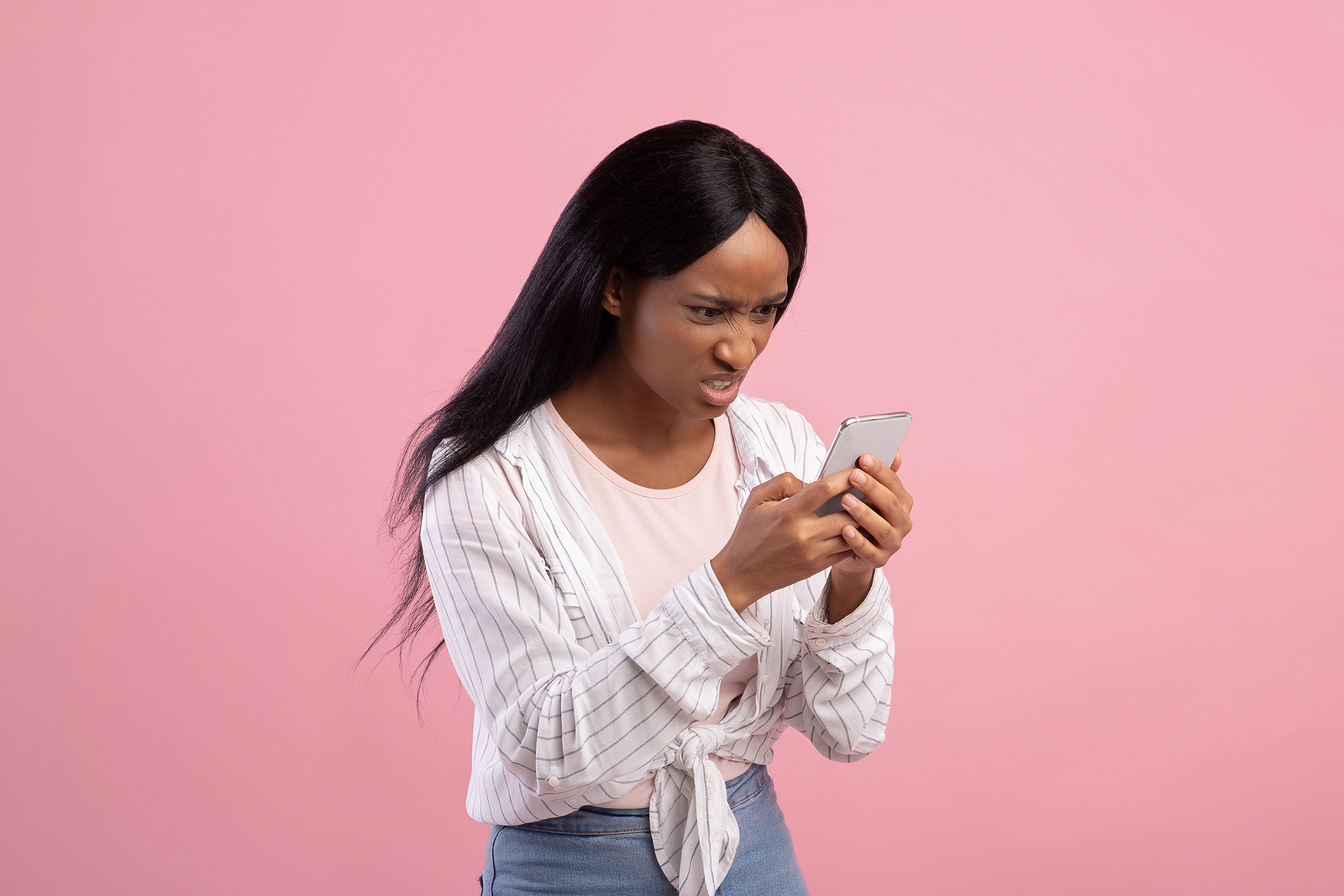 A woman looks frustrated at her phone against a plain background.