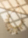 Statement gold necklace adorned with rectangular crystals, showcased in dappled sunlight against a neutral background.