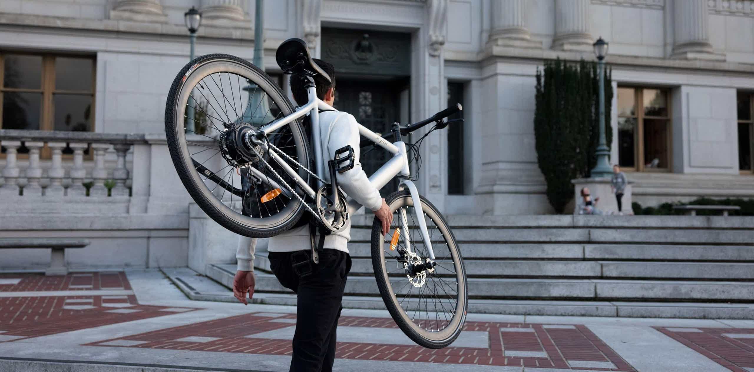 Imagen de recurso de un chico cargando con una bicicleta eléctrica sobre él.