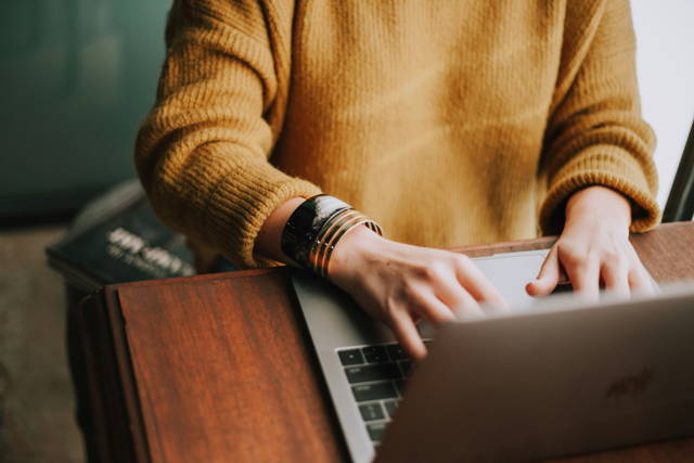 Mann in ockerfarbigem Pullover tippt auf Laptop