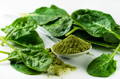 fresh spinach leaves spread around a spoon of green powder supplement